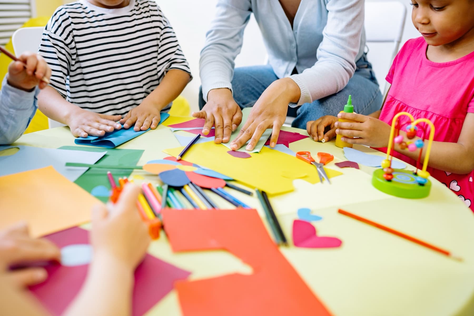 Children and a teacher making paper collages together at a low table